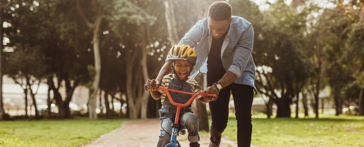Boy learning to ride a bicycle with his father in park. 