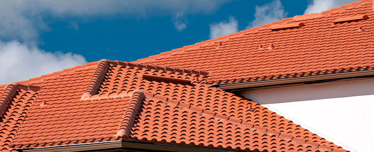 A white house featuring a red roof, representing a comparison between metal and clay roofing options for new homes.
