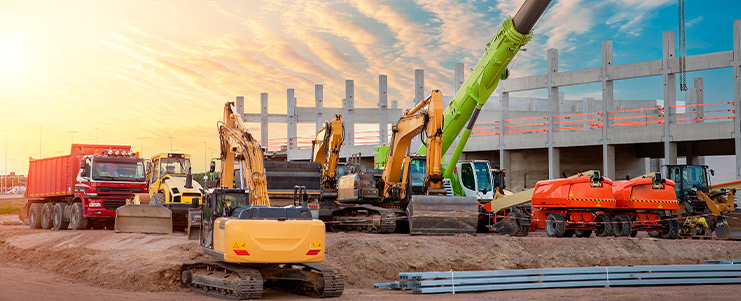 A variety of construction equipment, such as bulldozers and scaffolding, at an active construction site with workers present.