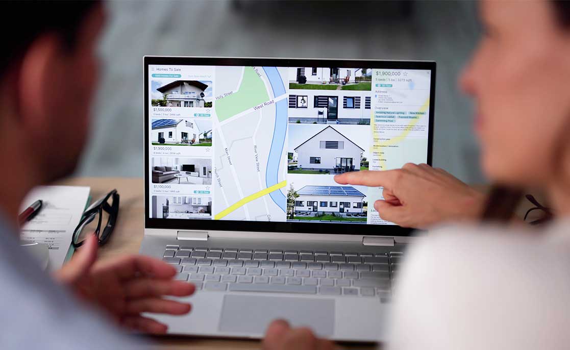 A man and woman examine a computer screen displaying a house, as they explore homebuilding options for first-time buyers.