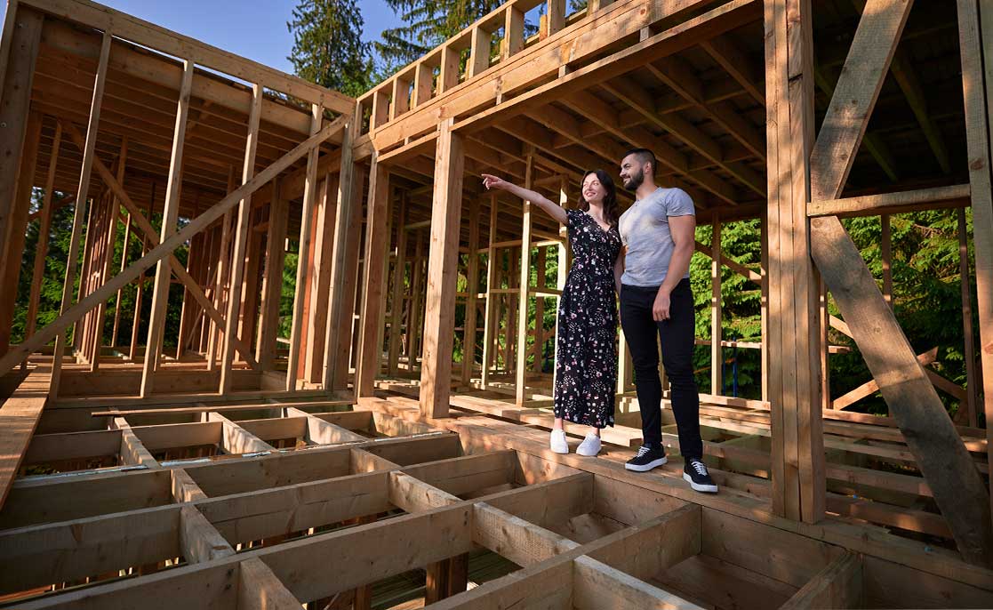A couple observes the construction site of their new home, engaged in conversation about the building process.